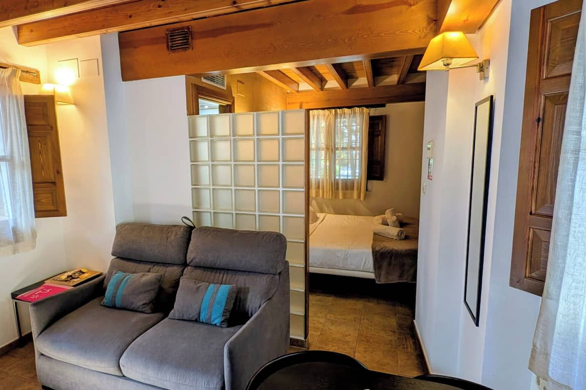 Una habitación acogedora con un sofá, una cama, un ventanal con cortinas y techo de madera.