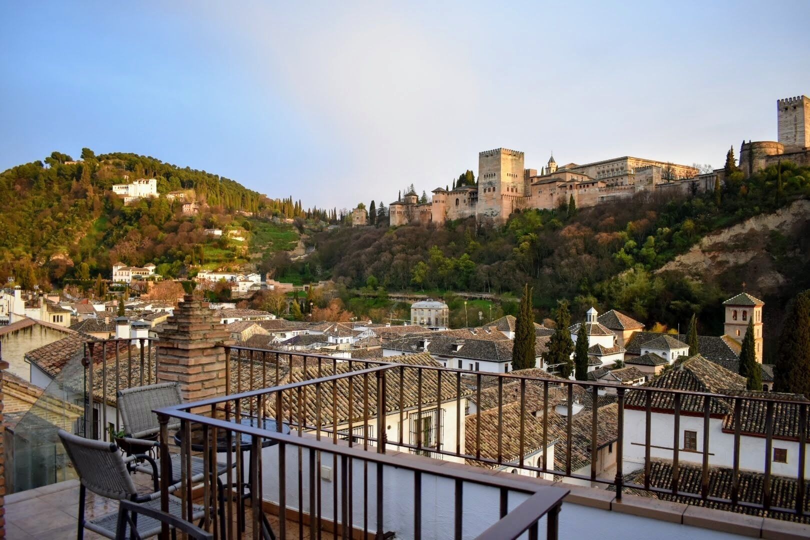 A view of a historic town with a prominent castle on a hill, terraced houses, and a balcony with wicker furniture.