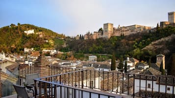 A view of a historic town with a prominent castle on a hill, terraced houses, and a balcony with wicker furniture.