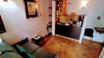 A compact living space with a kitchenette, a sofa, a small table, and a chair.
