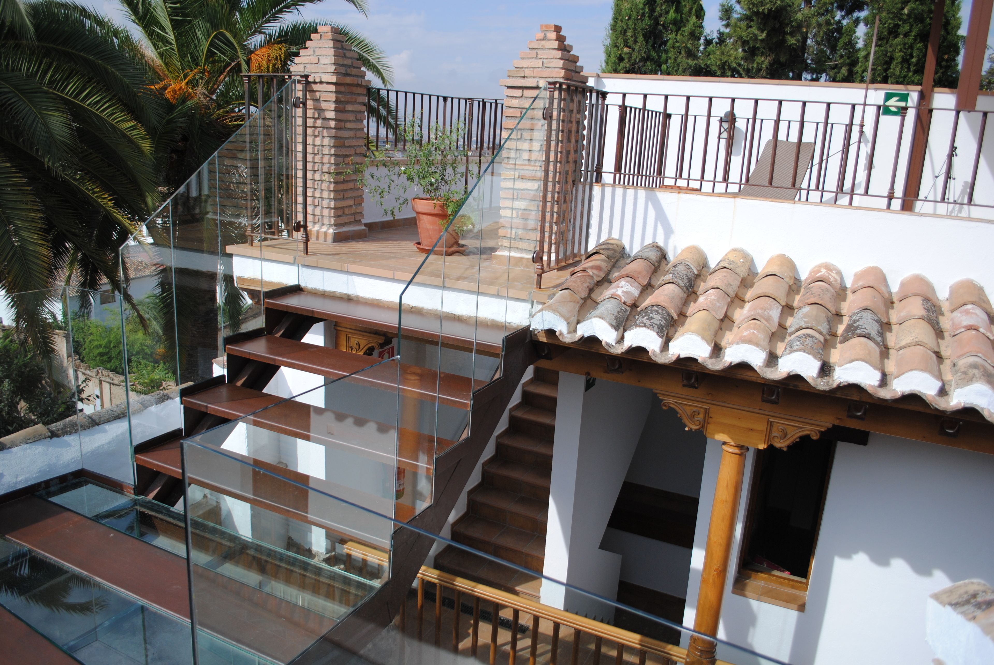 A multi-level residential building with a glass staircase, a tiled roof, and a brick wall.