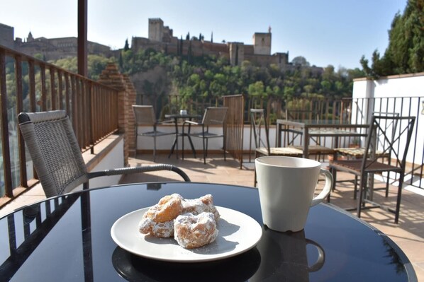 A table with a plate of pastries and a cup on a balcony overlooking a cityscape.