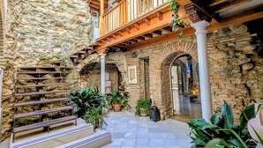 A stone courtyard with a wooden staircase, potted plants, and a wooden balcony. - Apartamentos Turísticos Alhambra (Granada)