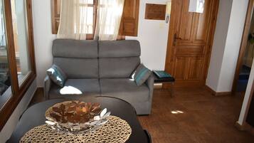 Ein Wohnzimmer mit grauem Sofa, einem kleinen Tisch mit dekorativer Schale und einer Holztür im Hintergrund.