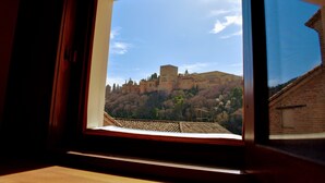 A view through a window of a historic building with a castle on a hill. - Apartamentos Turísticos Alhambra (Granada)