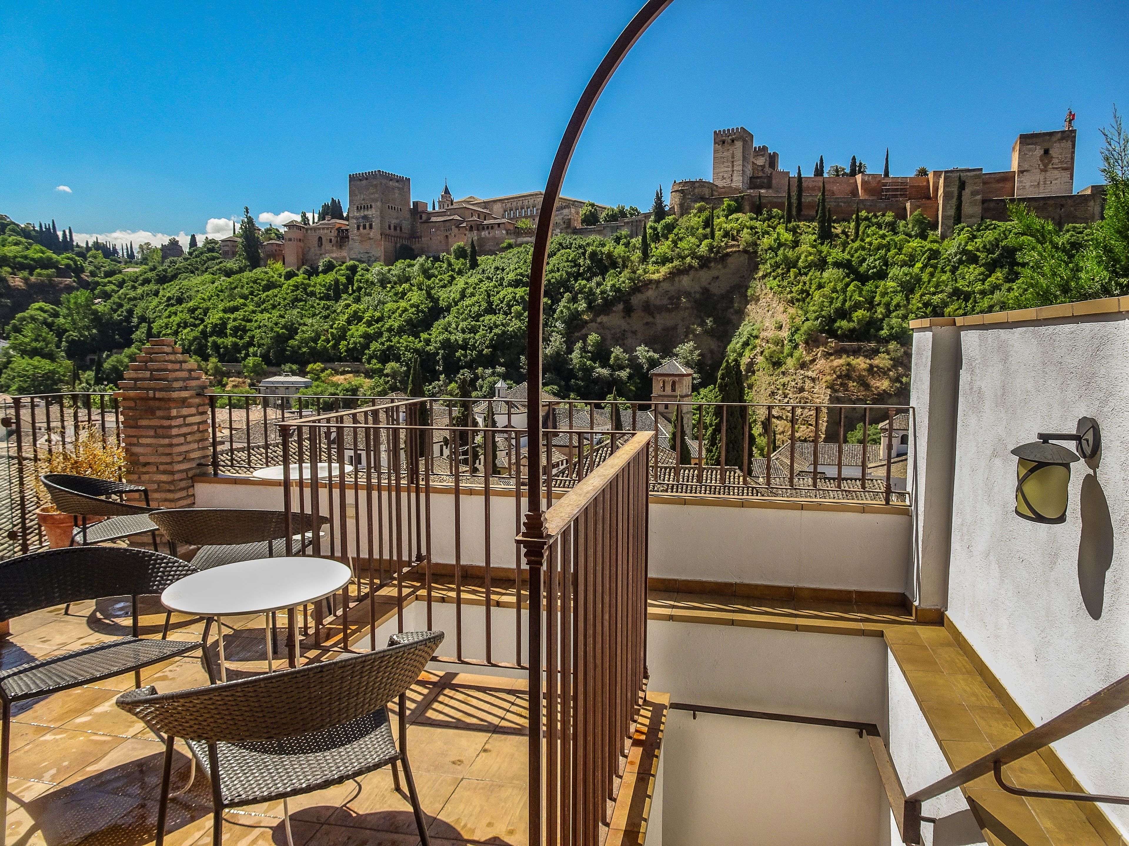 Una terraza con vistas a un castillo histórico, amueblada con sillas de mimbre y una mesa.