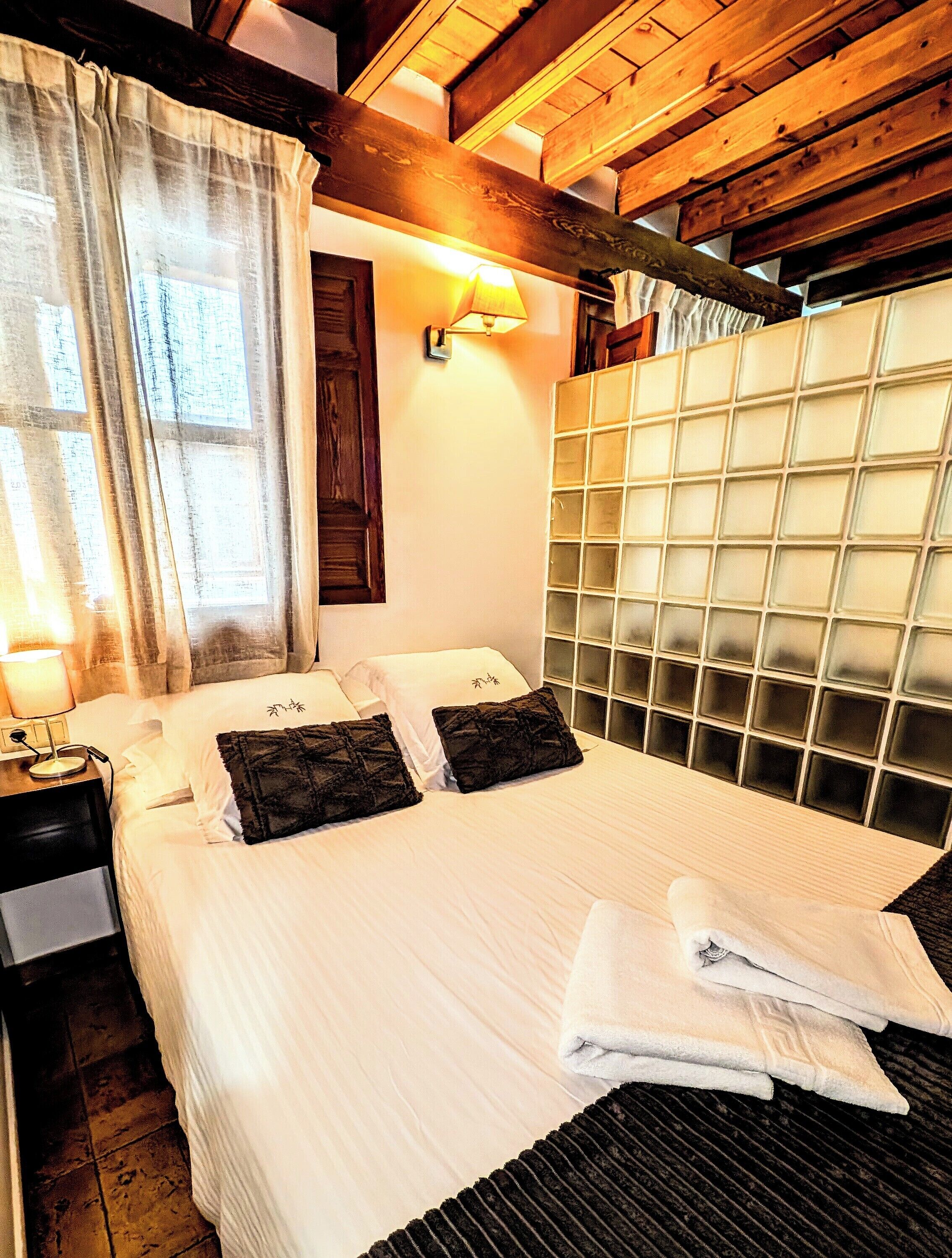 Una cama bien tendida con sábanas blancas, dos almohadas oscuras y un cabecero con diseño de panel de vidrio.