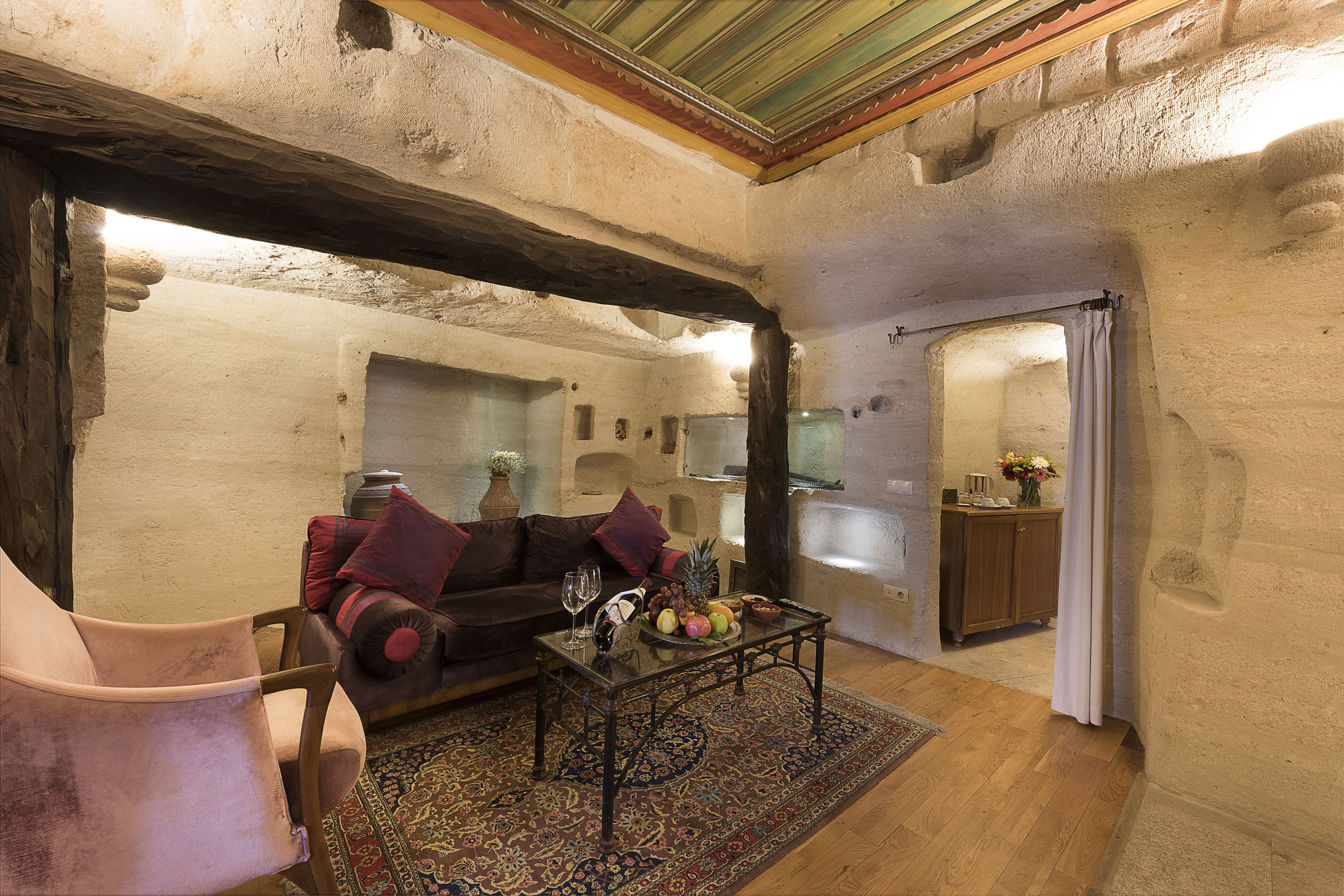Un interior rústico con techo de madera, un sofá con cojines, una mesa de centro con frutas y vasos, y una alfombra estampada.