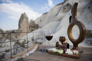 A wooden table with a cheese board, grapes, a wine glass, and a decorative bowl. - Anatolian Houses Cave Hotel & SPA (Nevsehir)