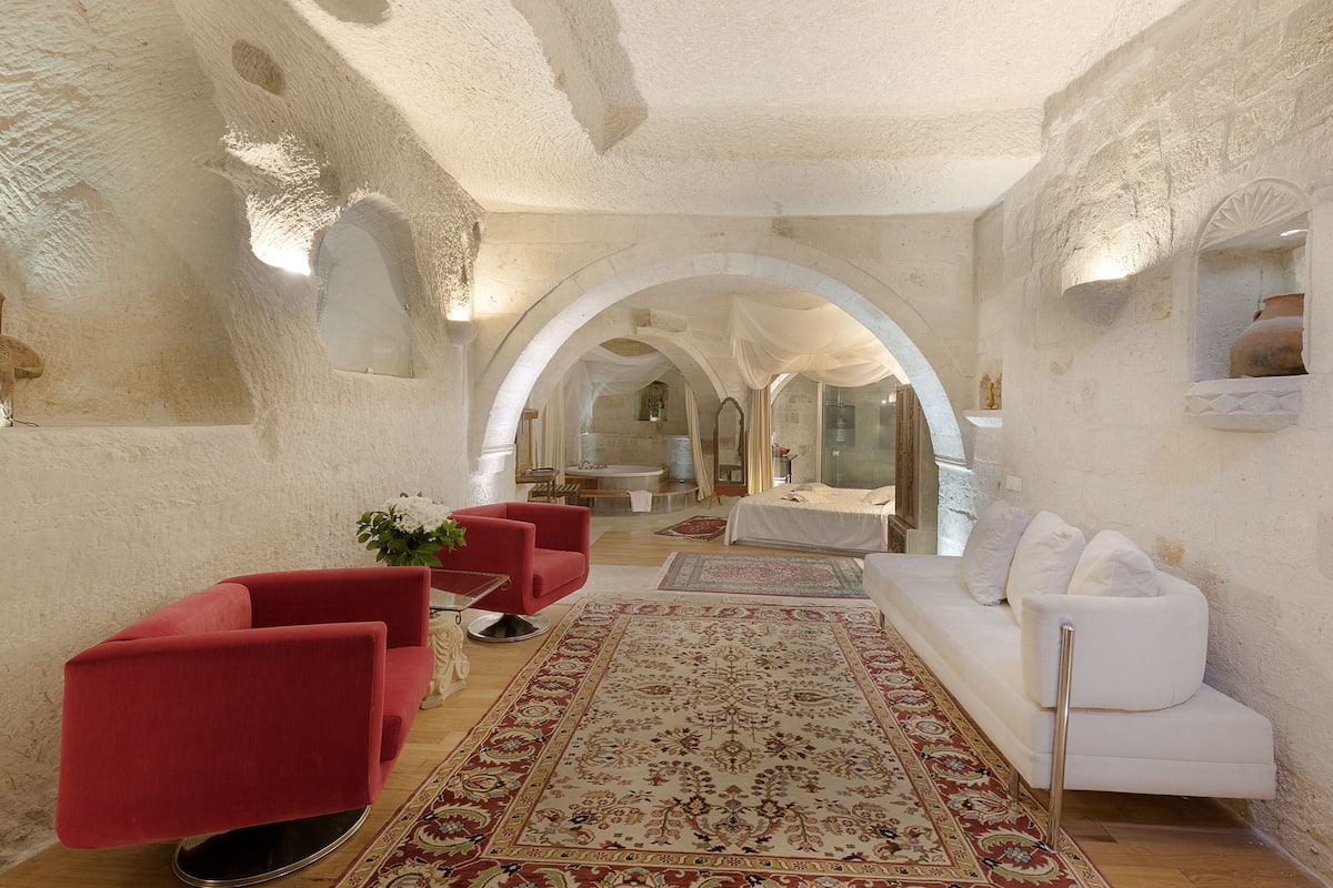 A spacious room with a white sofa, red armchairs, and a patterned rug.