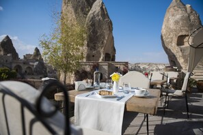 An outdoor dining area with a table set for two, a vase with yellow flowers, and a view of rock formations in the background. - Anatolian Houses Cave Hotel & SPA (Nevsehir)