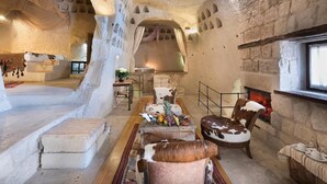 A rustic interior with stone walls, a fireplace, and a seating area with a table set for a meal. - Anatolian Houses Cave Hotel & SPA (Nevsehir)