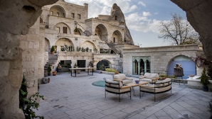 A courtyard with stone benches, a table, and a fireplace. - Anatolian Houses Cave Hotel & SPA (Nevsehir)
