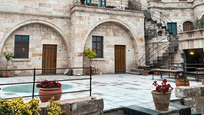A historic stone building with arched doorways and windows, a courtyard with steps, and potted plants. - Anatolian Houses Cave Hotel & SPA (Nevsehir)
