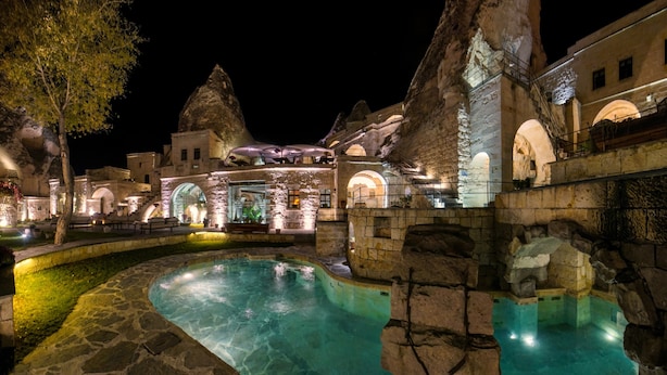 A nighttime view of a historic building with a pool, stone architecture, and illuminated interiors. - Anatolian Houses Cave Hotel & SPA (Nevsehir)