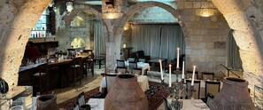 A restaurant with stone arches, tables set with candles, and a bar area visible through the arches.