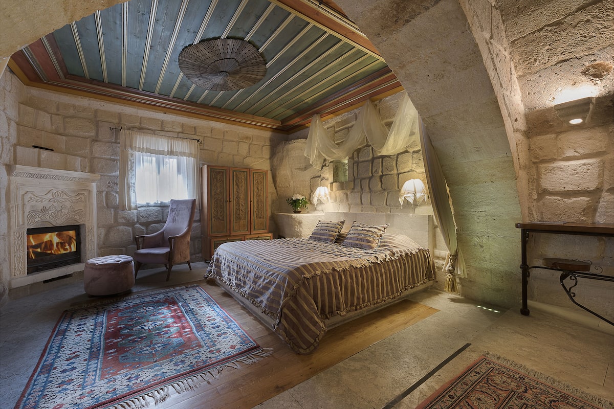 A bedroom with a stone fireplace, a large bed, and a wooden ceiling.