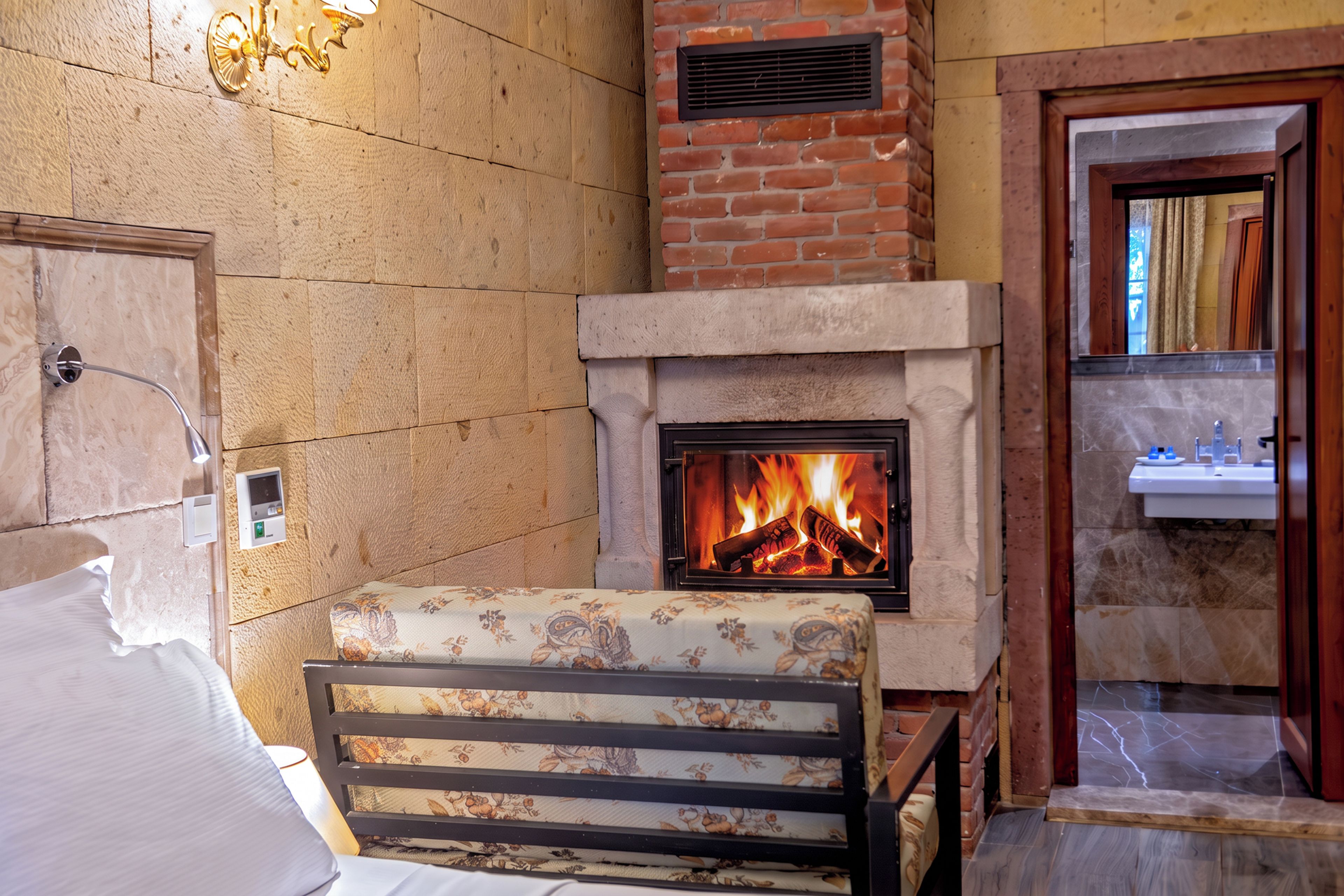 Una habitación con chimenea, una cama con cubrecama floral y un baño visible a través de una puerta abierta.