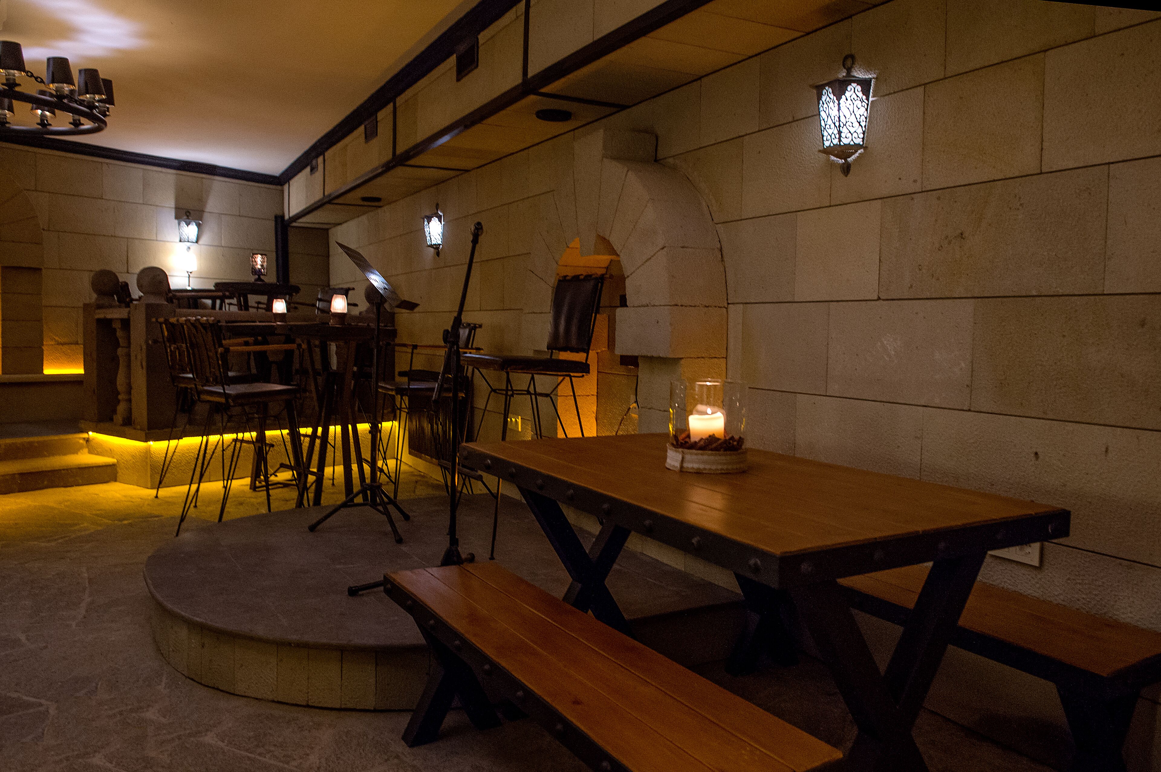 A cozy restaurant with stone walls, wooden tables, and benches. There are candles on the tables and a stone oven in the background.
