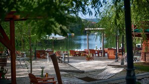 An outdoor patio area with wooden furniture, a hammock, and a view of a lake. - Wineport Lodge Agva (Sile)