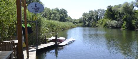 A wooden dock with a sign for Wineport Lodge, a boat docked at the pier, and a river surrounded by greenery.