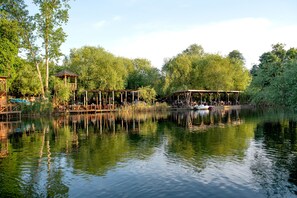 A riverside park with wooden structures, a boat, and lush greenery. - Wineport Lodge Agva (Sile)