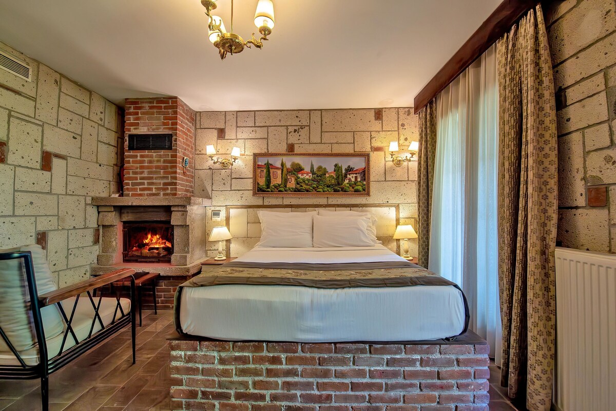 A room with a brick fireplace, a bed with white bedding, a wooden bench, and a painting on the wall.