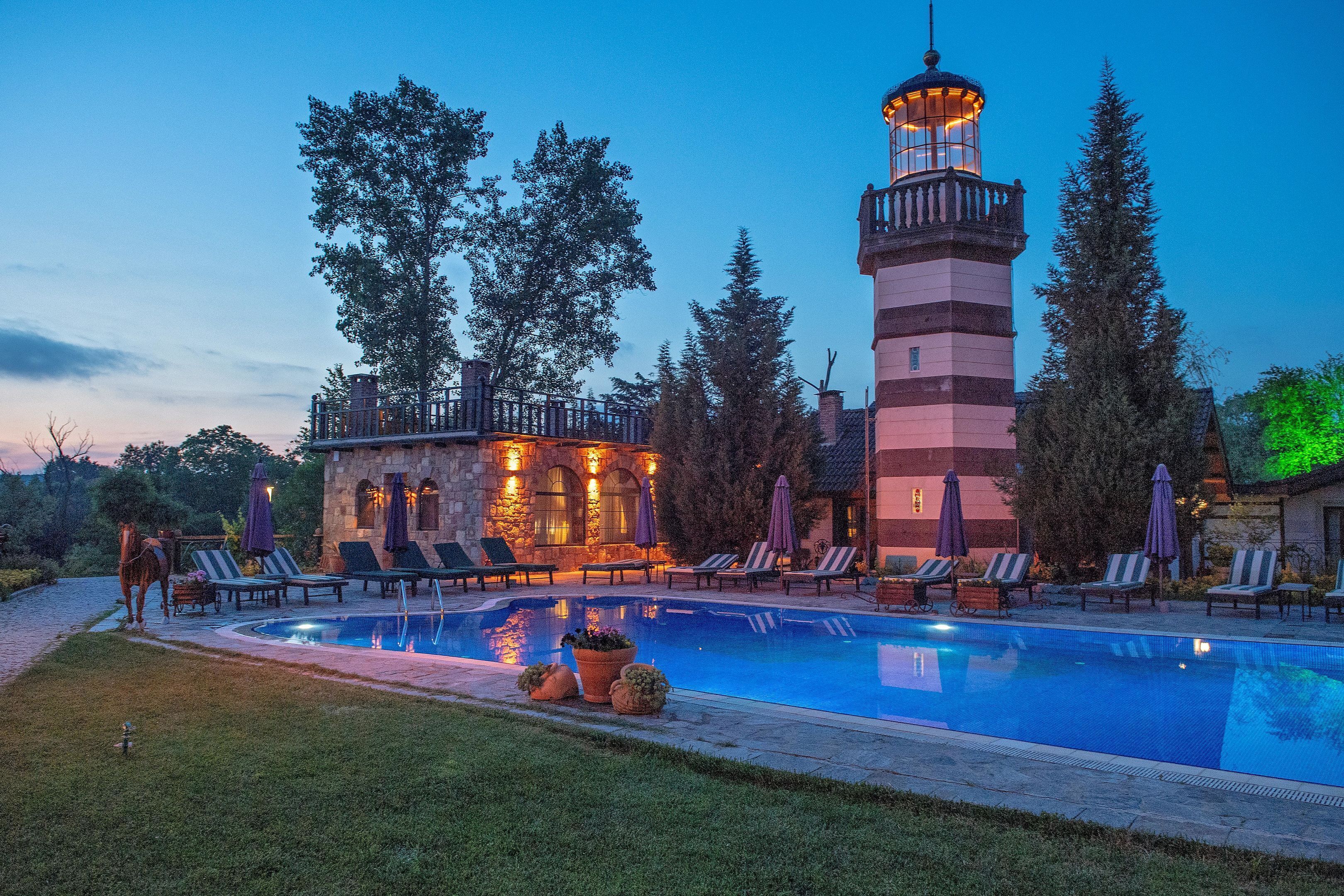 Zona de piscina con sillones de descanso y un edificio de piedra con motivos de faro.