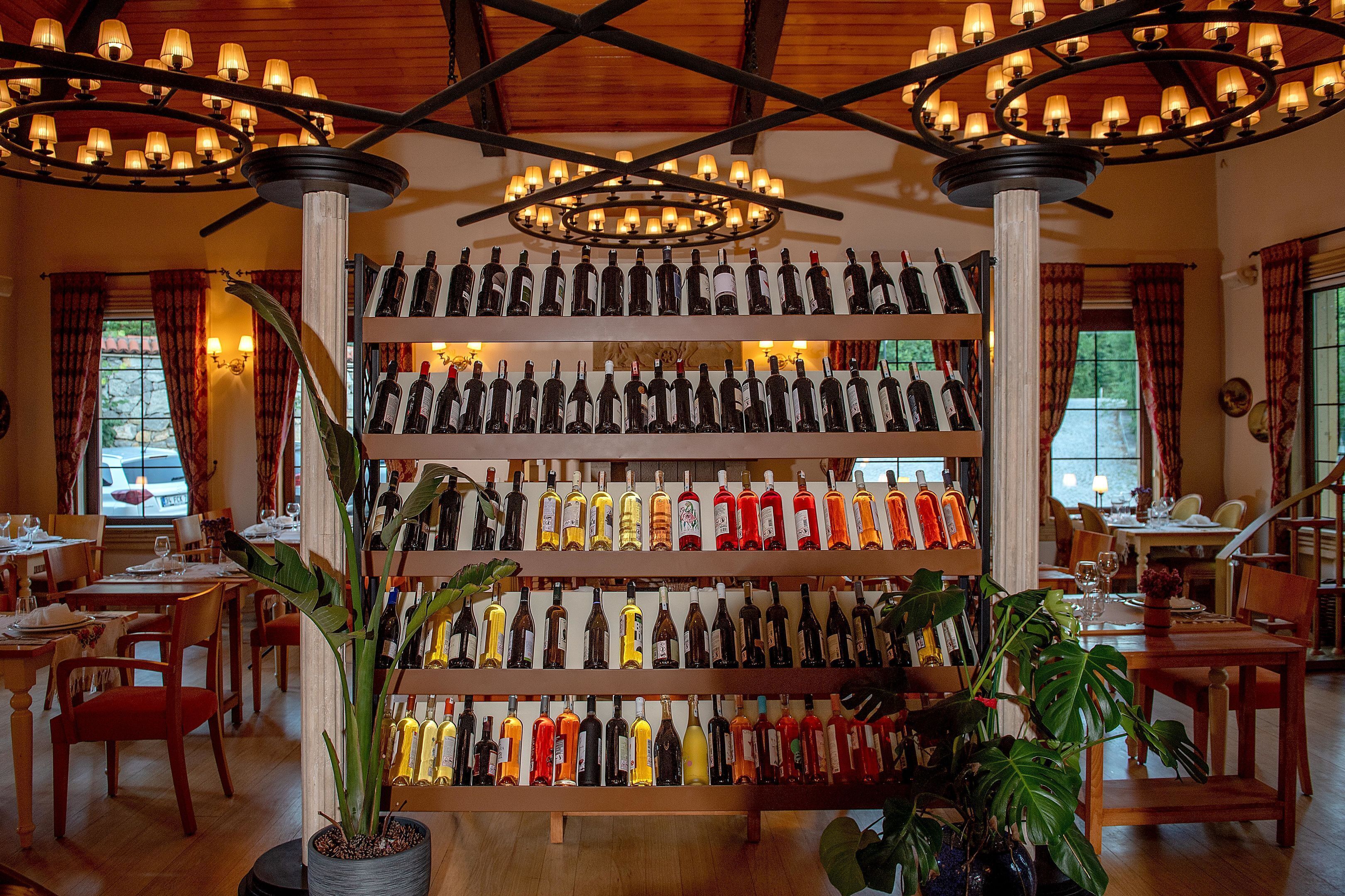 A restaurant with multiple dining tables, chairs, and a large wine rack with various bottles.