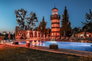 A pool area with lounge chairs and a fountain, surrounded by trees and a stone building with a tower. - Wineport Lodge Agva (Sile)