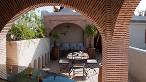 An outdoor patio with a round table and chairs, surrounded by brick arches, and a view of a building with a white facade and a dome. - Riad Granvilier (Marrakech)