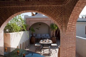 Un patio al aire libre con una mesa redonda y sillas, rodeado de arcos de ladrillo, y vistas a un edificio de fachada blanca y cúpula.