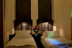 A hotel room with two single beds, a nightstand with a vase of flowers, and wall-mounted lamps. - Riad Granvilier (Marrakech)