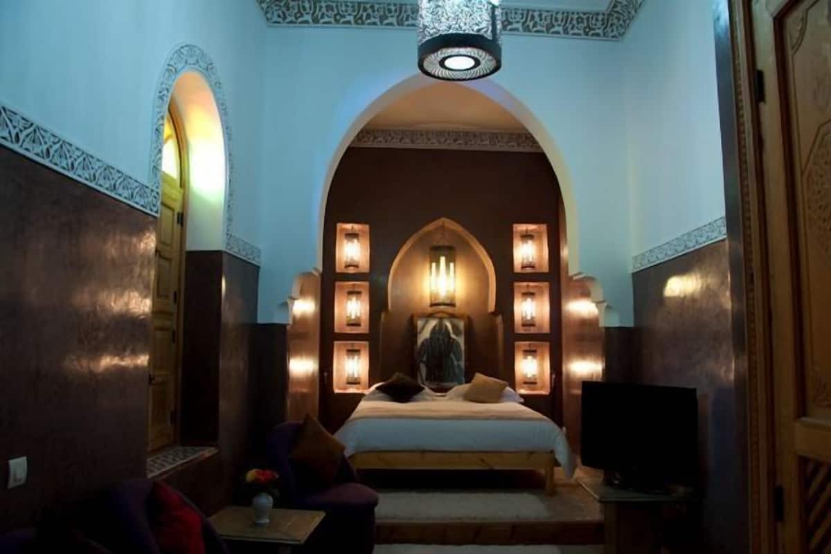 A bedroom with a large bed, a TV, and multiple wall-mounted lights.