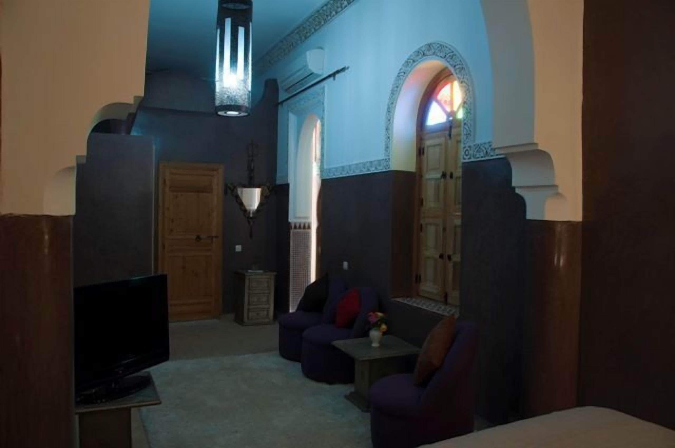 Una sala de estar con televisor, zona de descanso y un arco decorativo.