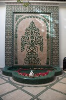 Pared de azulejos con intrincados diseños verdes y una fuente circular con pétalos de rosa.