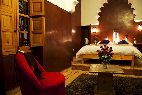 A bedroom with a wooden bed, a red chair, and a small table with a vase of flowers. - Riad Granvilier (Marrakech)