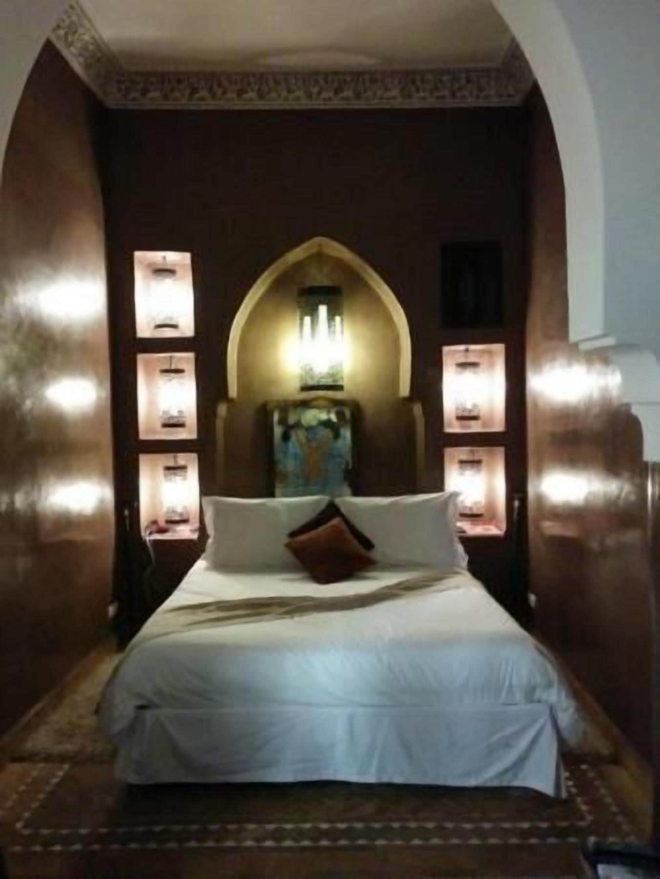 Quarto com cama grande, arco decorativo e iluminação na parede.