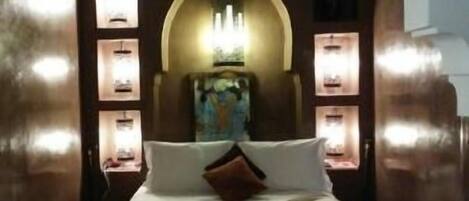 Quarto com cama grande, arco decorativo e iluminação na parede.