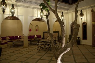 Un interior tradicional marroquí con arcos, una zona central de comedor y faroles colgantes.