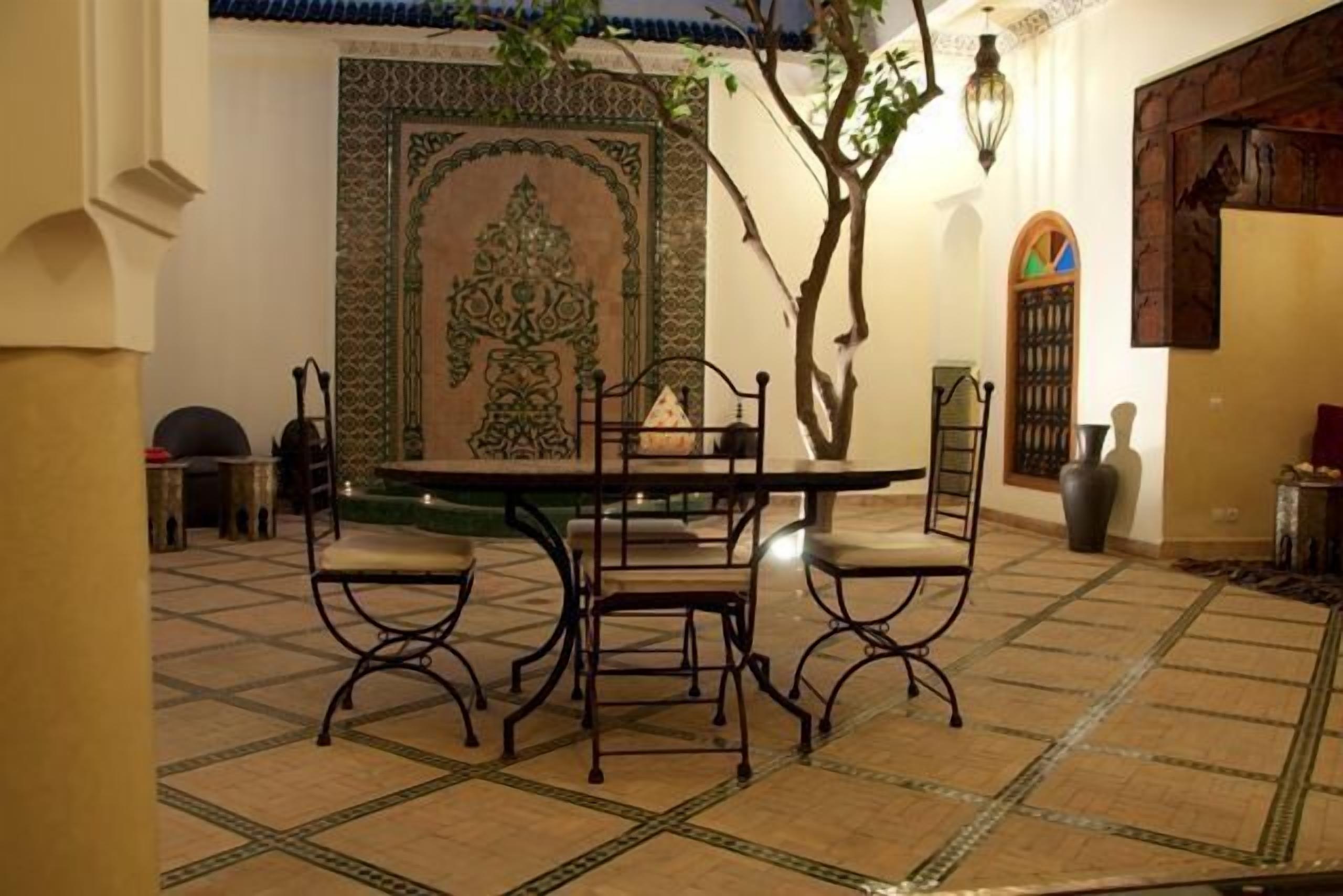 An indoor courtyard with a tiled floor, a round table with chairs, and a decorative wall with intricate patterns.