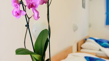 A room with a bed, a wooden table, and a purple orchid plant in a pot.