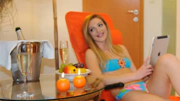 A room with a glass table holding a champagne bottle, a glass, and a bowl of fruit.