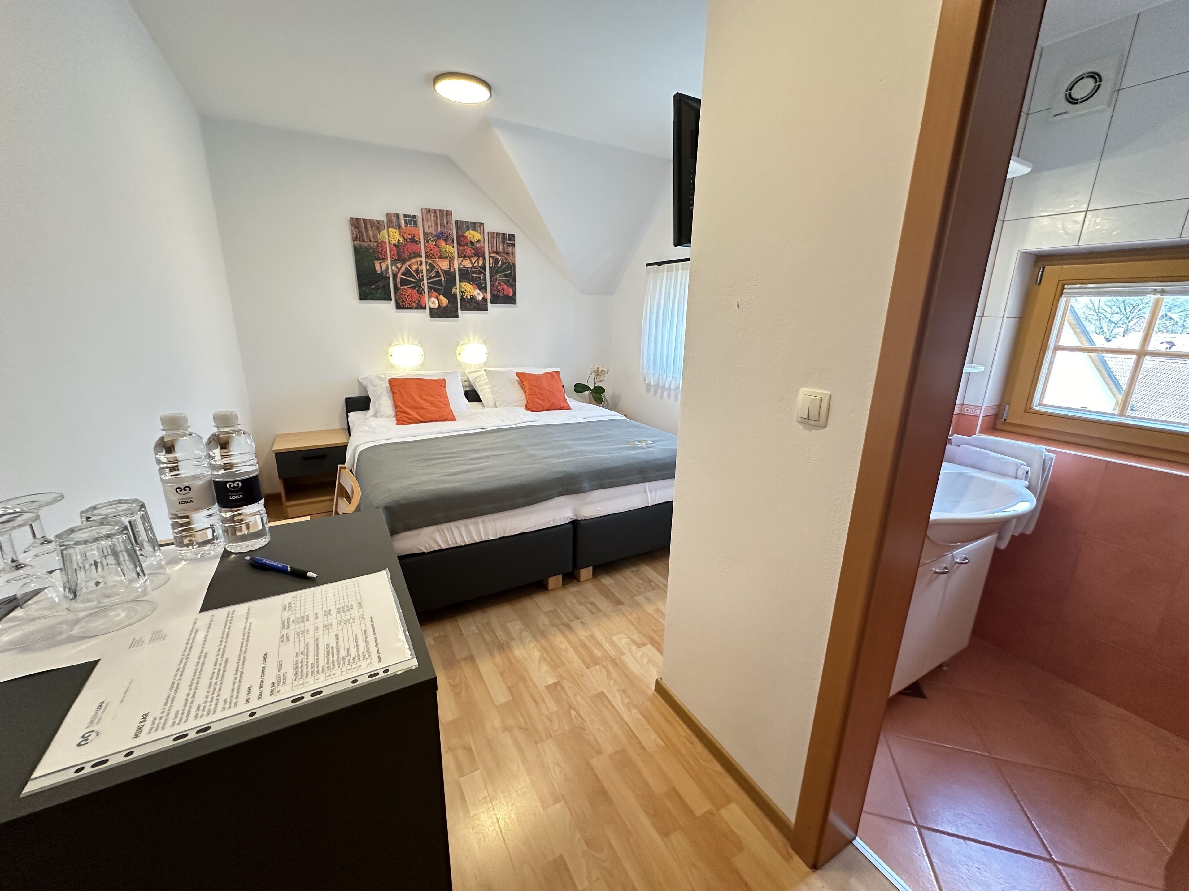 Un dormitorio con cama, mesitas de noche, un escritorio con un menú y una ventana.