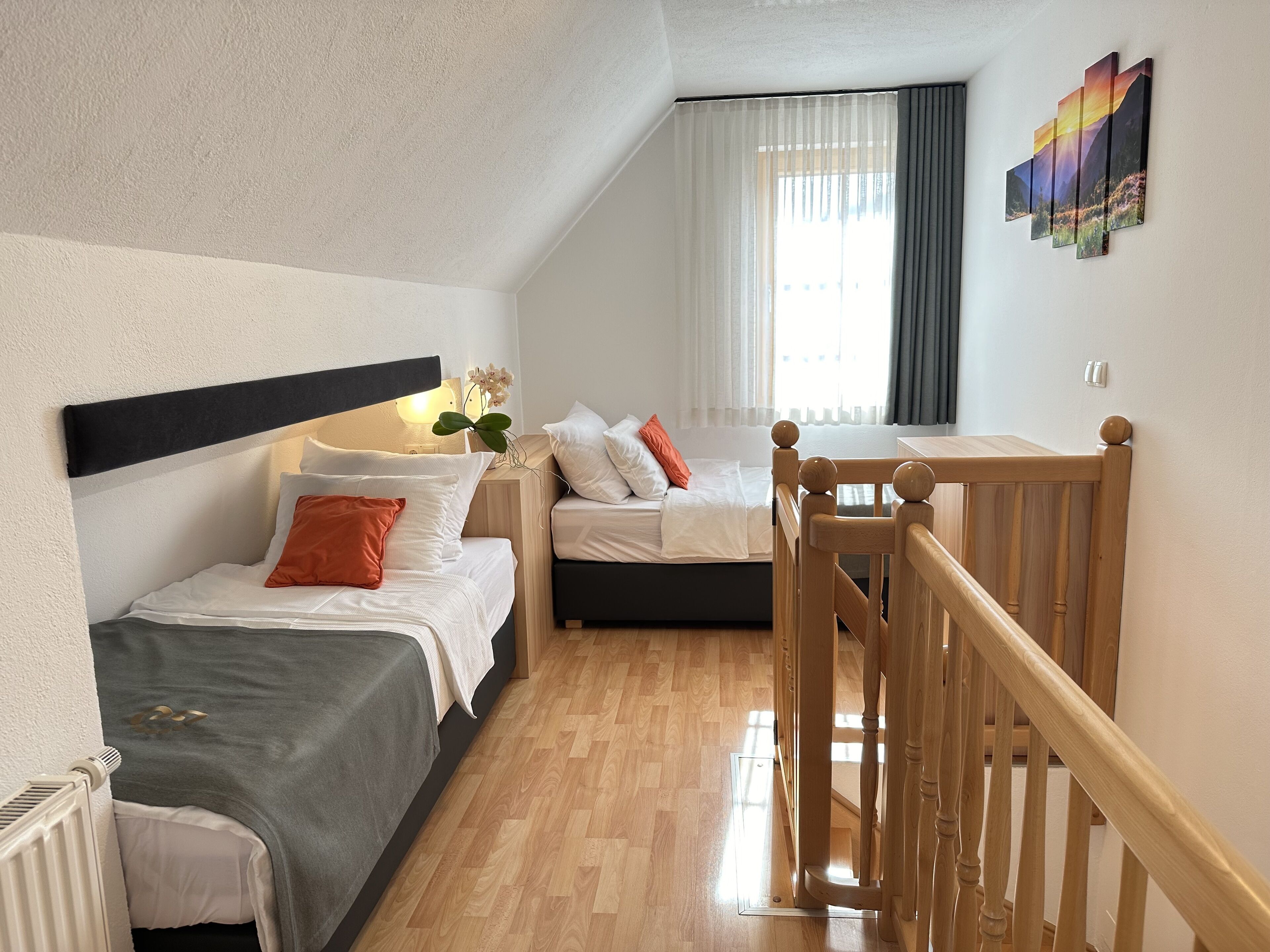 A modern hotel room with a wooden floor, two beds, a wooden headboard, a nightstand with a lamp, and a window with curtains.