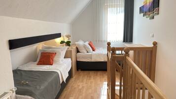 A modern hotel room with a wooden floor, two beds, a wooden headboard, a nightstand with a lamp, and a window with curtains.
