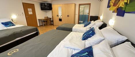 A hotel room with two single beds, a desk, and a shower area.