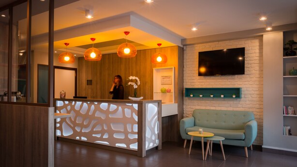 A modern reception area with a wooden reception desk, a green sofa, and a flat-screen TV mounted on a brick wall. - Reims Hotel (Paris)