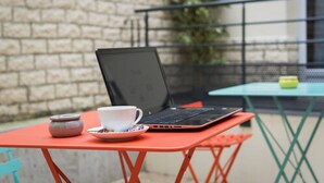 A laptop on a red table with a cup and saucer, a small pot, and a green table in the background. - Reims Hotel (Paris)