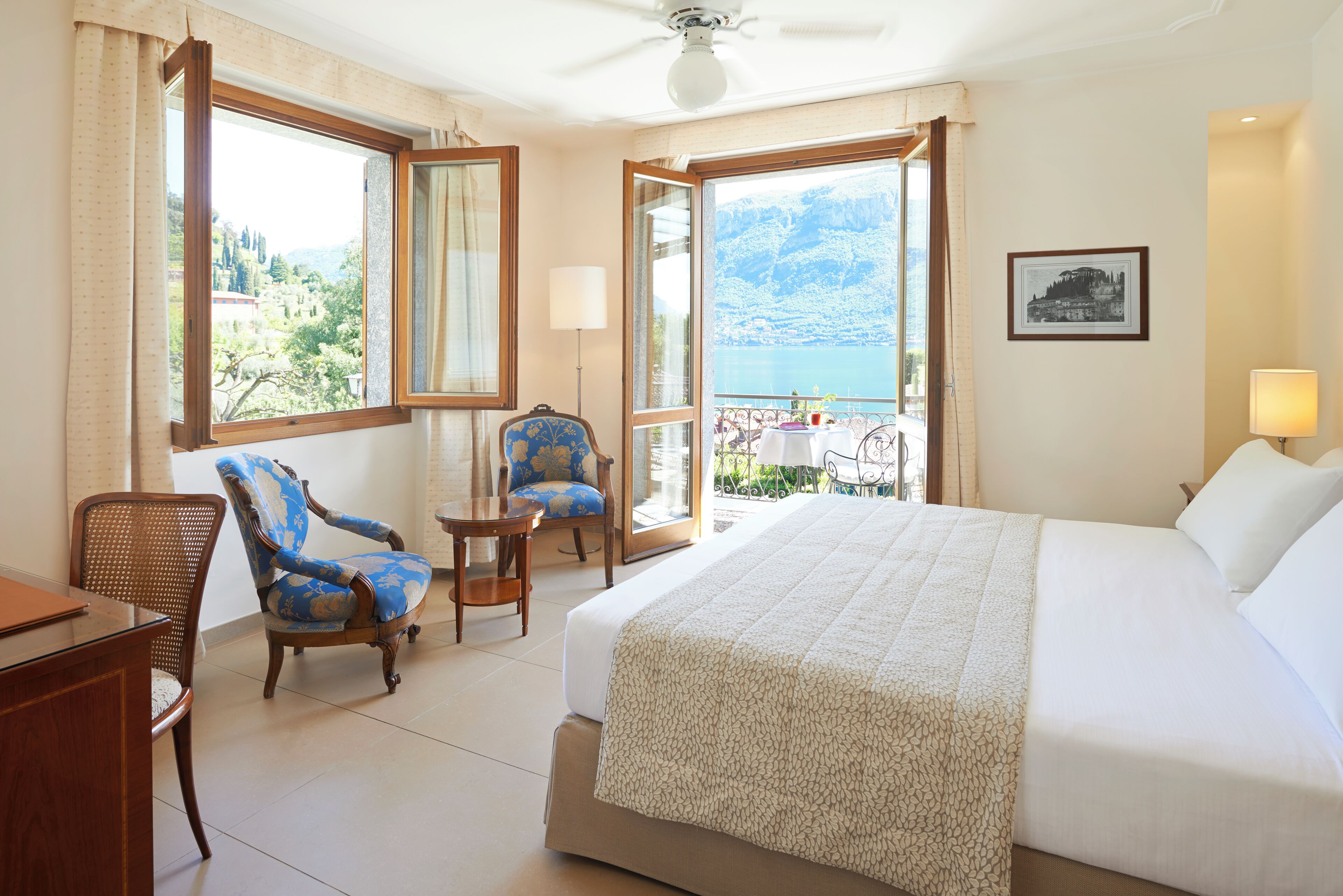 A hotel room with a large bed, a chair, a small table, and a balcony with a view of the sea.